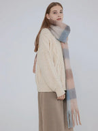 Side view of a woman wearing a cream cable knit sweater and a plaid scarf.