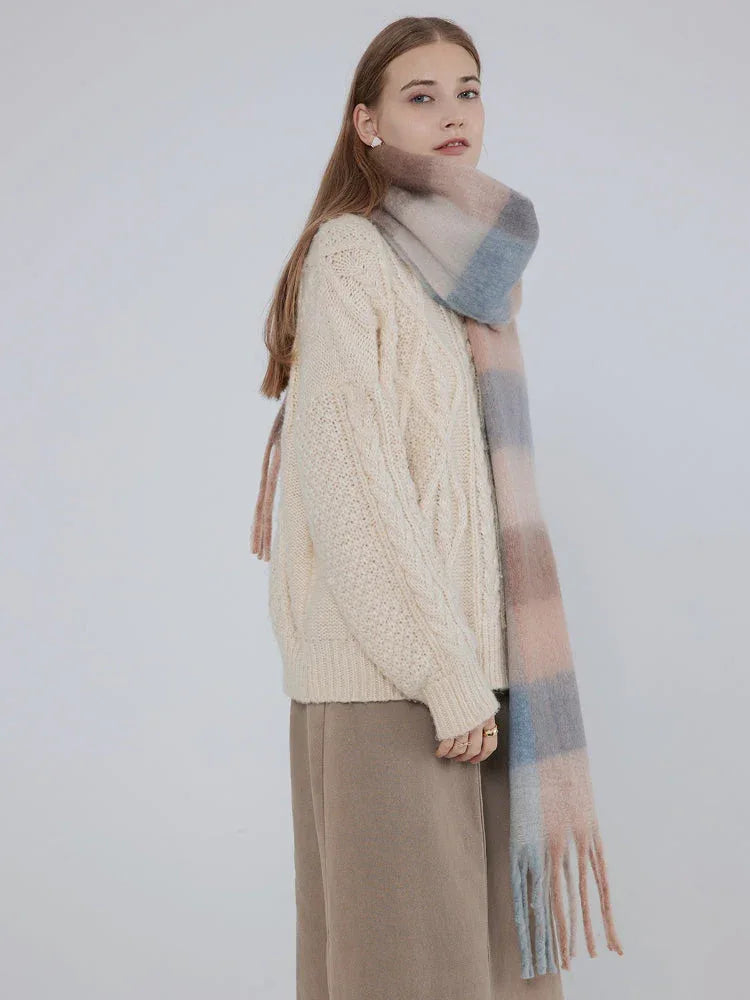 Side view of a woman wearing a cream cable knit sweater and a plaid scarf.