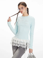Close-up of a woman wearing a light blue long-sleeve top with white lace trim and grey wide-leg jeans, adjusting her braided hair.