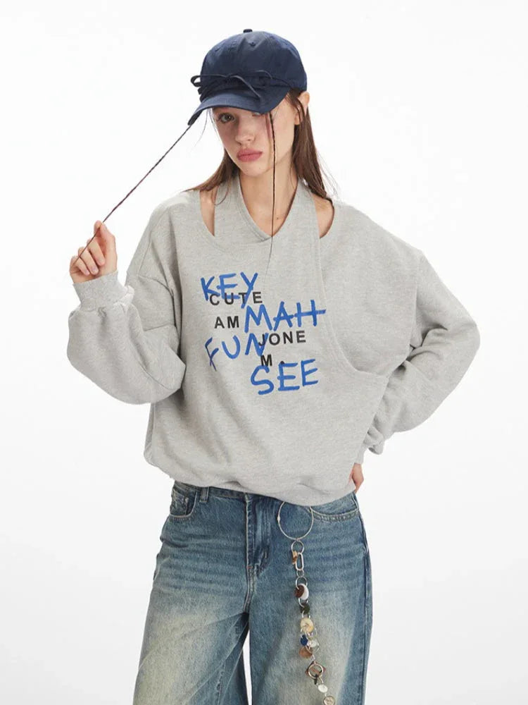 Model wearing a grey graphic print sweatshirt and wide-leg jeans, posing with her hands on her hat
