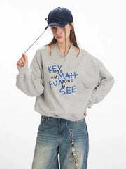 Model wearing a grey graphic print sweatshirt and wide-leg jeans, posing with her hands on her hat
