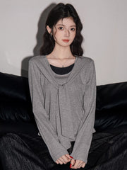 Woman wearing a grey long-sleeved top with a draped overlay and black pants, sitting on a black couch.