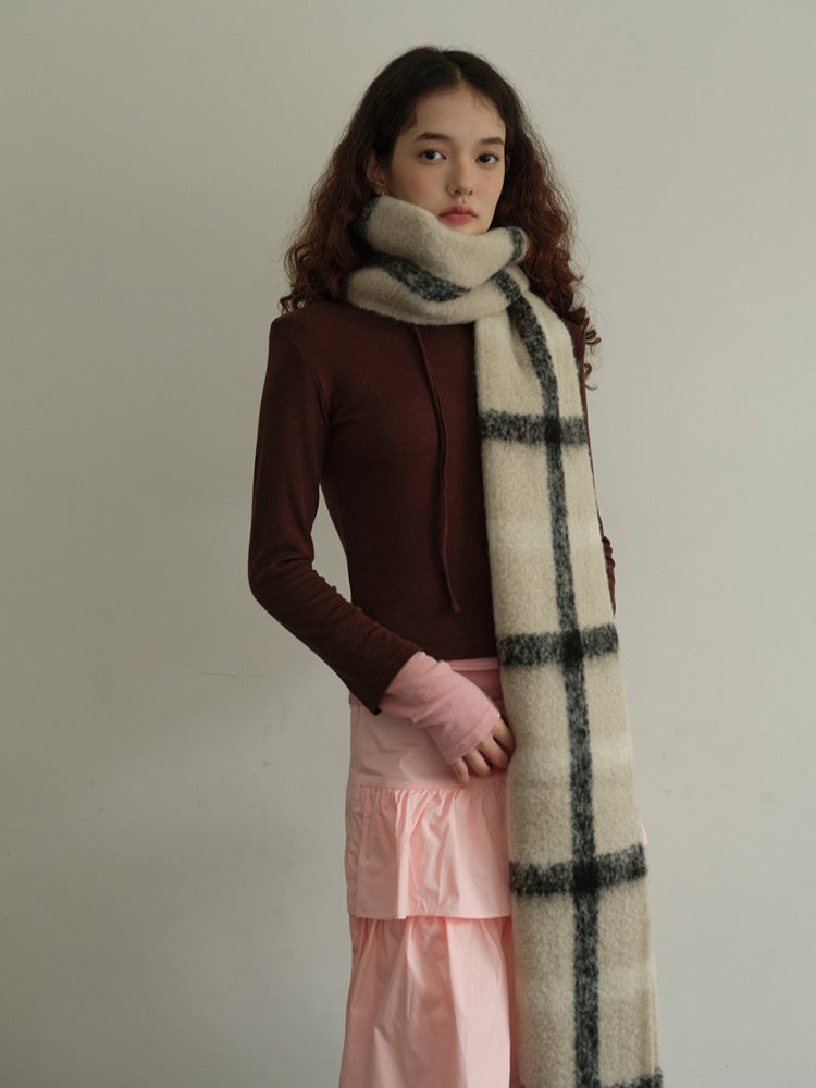 Full body shot of a model in a brown long-sleeved top, pink tiered skirt, and a cream and black plaid scarf. Secondary image