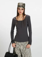 Close-up front view of a woman wearing a dark grey long-sleeve top with a square neckline and button details, paired with wide-leg grey leopard print pants. She is holding a dark handbag and wearing a patterned headscarf.