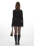 Back view of a woman wearing a black turtleneck sweater with fringe details, a fur-trimmed belt, star pattern hosiery, and black boots.