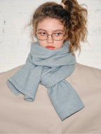 Close-up of the model's face and upper body, showing the light blue scarf wrapped around her neck and the details of the beige coat.
