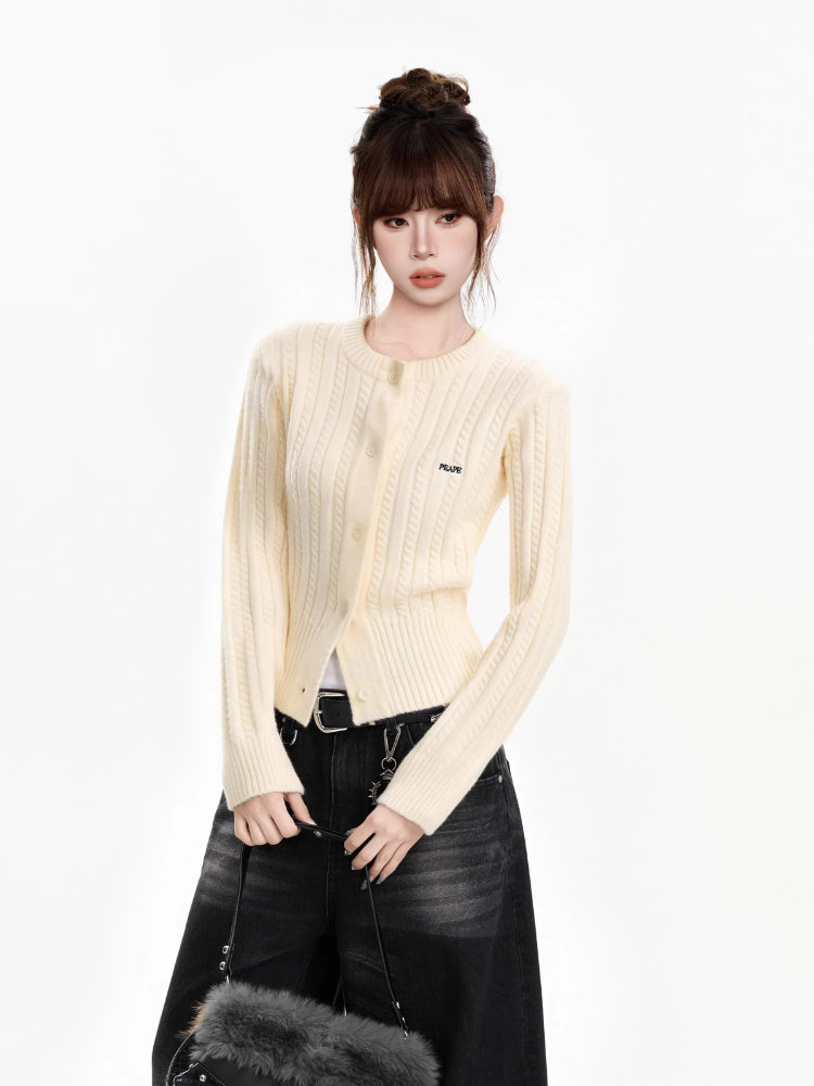 Woman wearing a cream cable knit cropped cardigan with black jeans and a black belt, holding a black fur bag