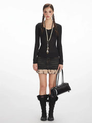 Woman wearing a black long-sleeved top, denim mini skirt with fur trim, and black knee-high boots, holding a black shoulder bag.
