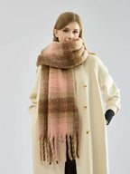 Woman wearing a cream-colored coat and a large plaid scarf in shades of pink and brown.