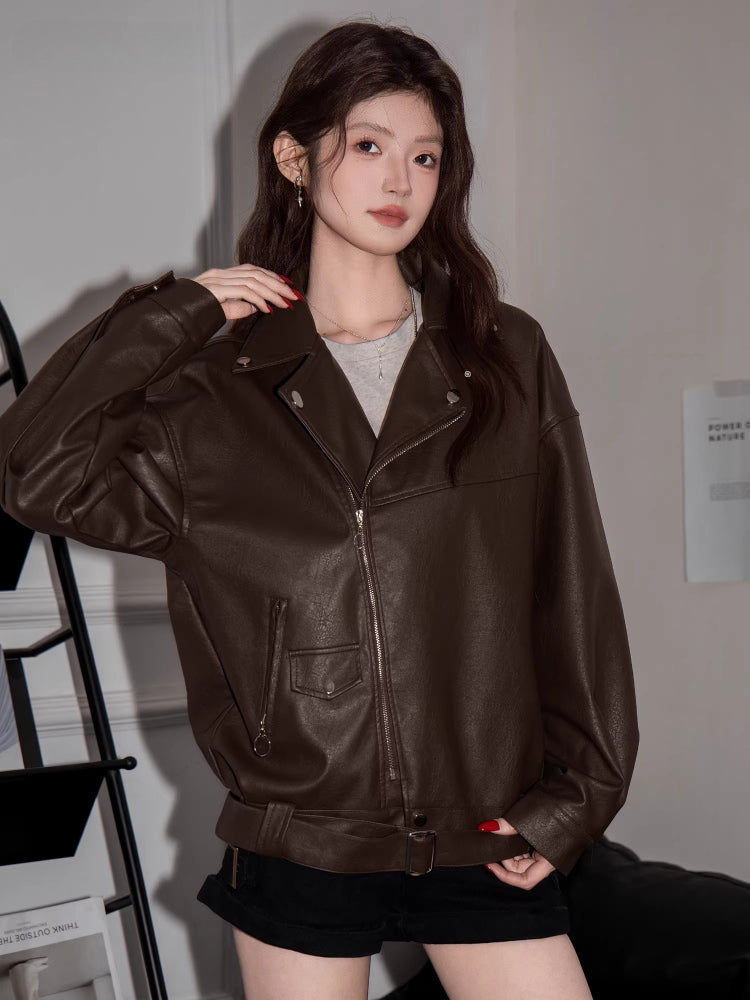 Close-up of a woman wearing a brown faux leather moto jacket with a grey crop top.