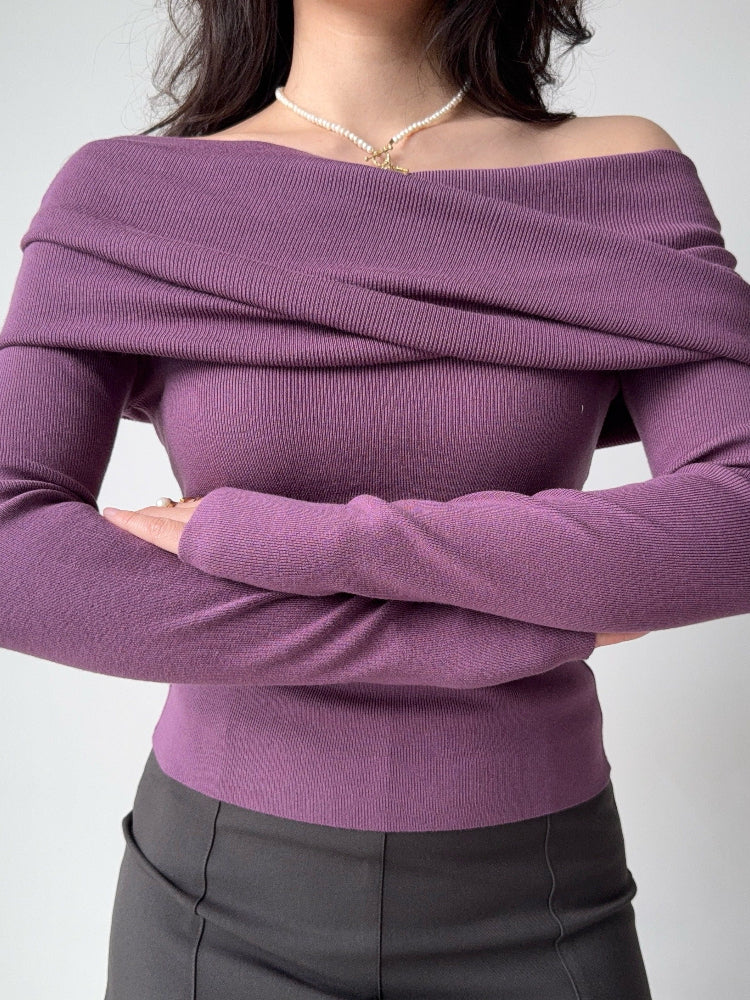 Woman wearing a purple off-the-shoulder knit top with long sleeves and a draped neckline, arms crossed.