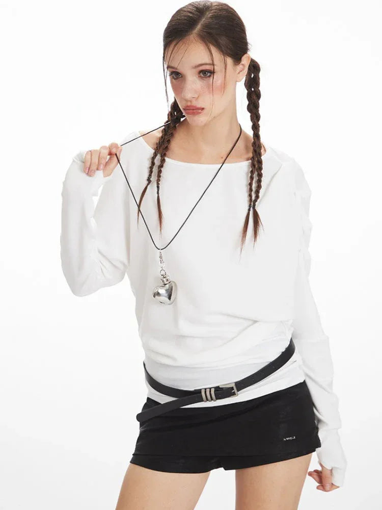 Close-up of a model wearing a white off-the-shoulder long-sleeve top, black high-waisted shorts, black belt, and black knee-high socks, holding her braided hair.