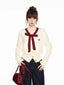 Woman wearing a cream-colored cardigan with a burgundy bow and trim, dark wash wide-leg jeans, and a burgundy handbag.
