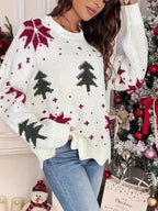 Woman standing in front of a Christmas tree, wearing a white knitted sweater with a Christmas tree and snowflake print.