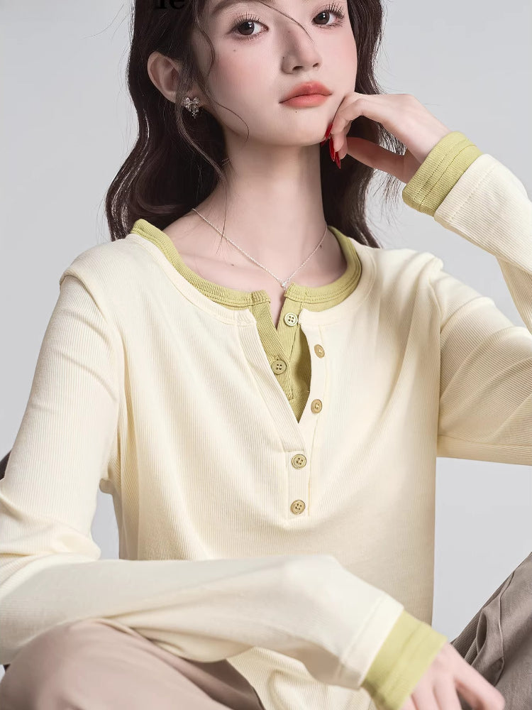 Close-up of a woman wearing a cream long-sleeved shirt with green trim and buttons.