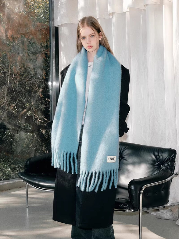 Full body shot of a woman wearing a light blue fluffy knit scarf with fringe detail and a black coat.
