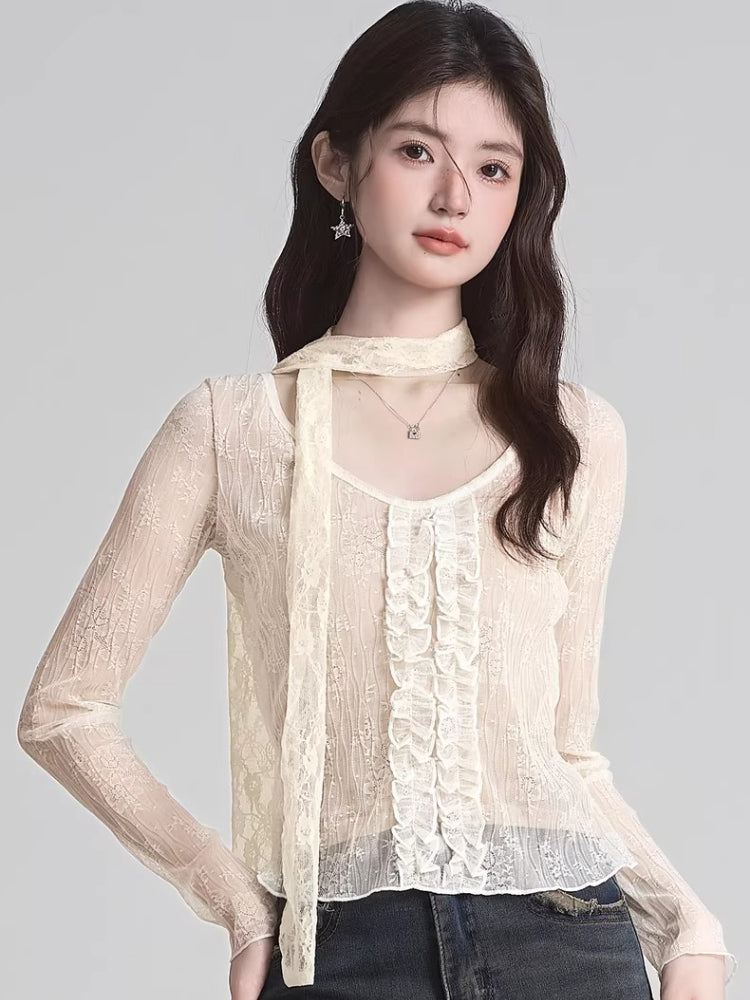 Woman wearing a cream-colored sheer lace long-sleeve top with ruffle detailing and a scarf detail.
