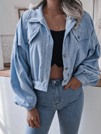 Woman wearing a light blue corduroy cropped jacket with balloon sleeves, standing with her hand in her pocket.