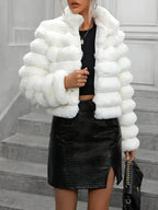 Woman holding a black handbag and wearing a white faux fur cropped jacket, black top, and black skirt.