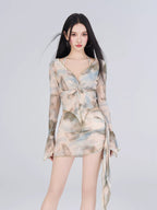Woman wearing a sheer mesh two-piece set with an abstract print, featuring a twisted v-neck long-sleeve top and a ruched mini skirt.