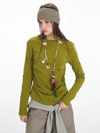 Close-up of a woman wearing a green long-sleeved top, taupe wide-leg pants, and yellow handbag, with a striped headband.