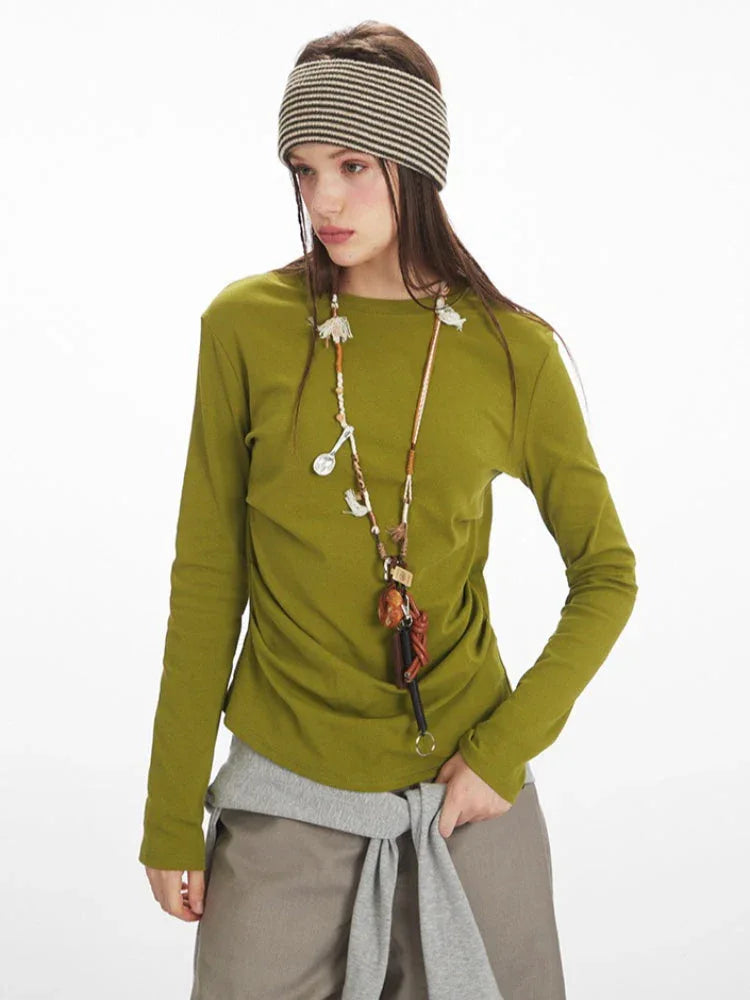 Close-up of a woman wearing a green long-sleeved top, taupe wide-leg pants, and yellow handbag, with a striped headband.