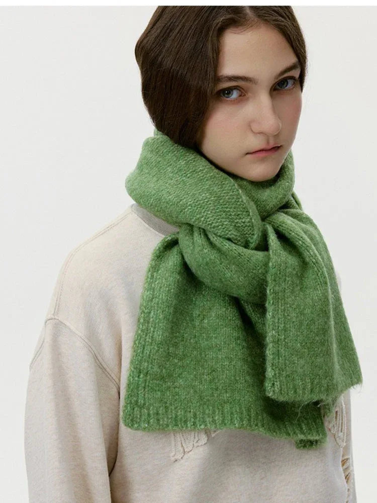 Model wearing a cream sweatshirt and a thick green knit scarf wrapped around her neck, three-quarter view.