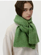 Model wearing a cream sweatshirt and a thick green knit scarf wrapped around her neck, three-quarter view.
