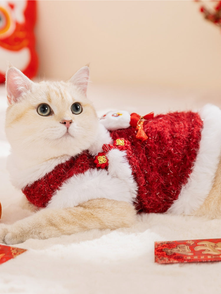 A cream-colored cat lying down, wearing a red and white festive vest with a lion dance embellishment.