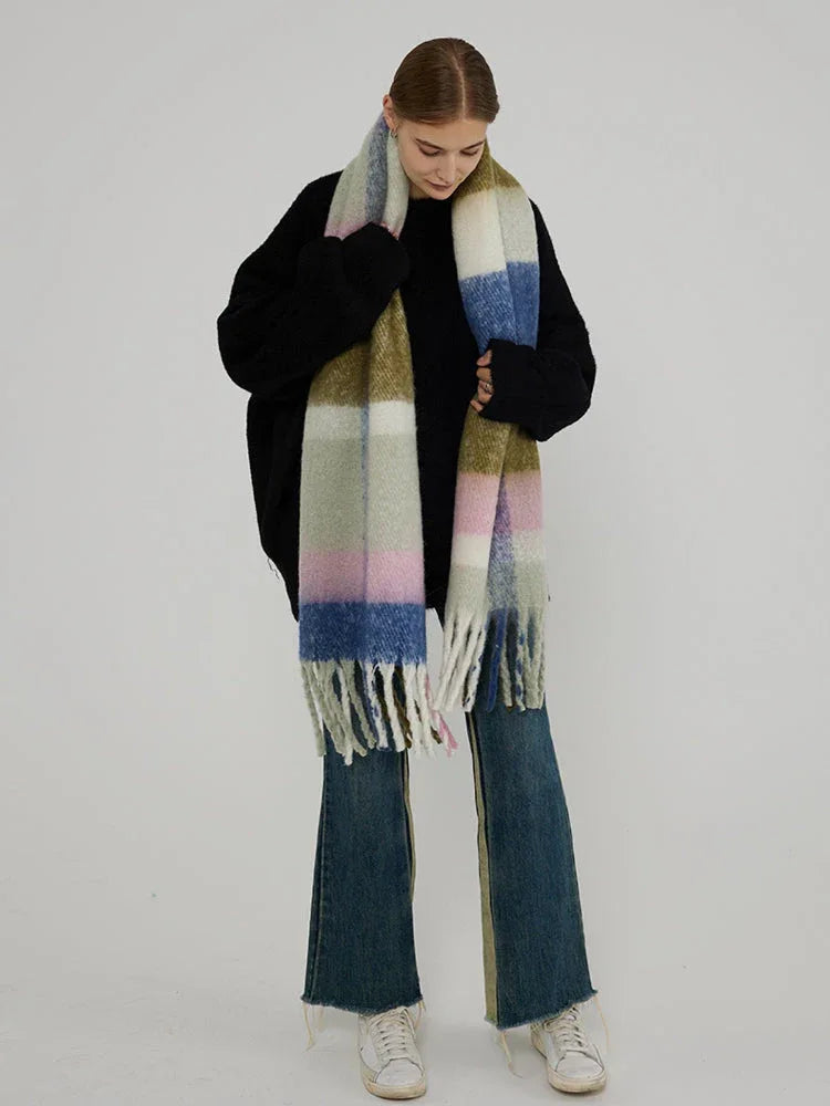 Woman in a black sweater and jeans, holding a large plaid scarf with green, pink, blue, and white blocks.