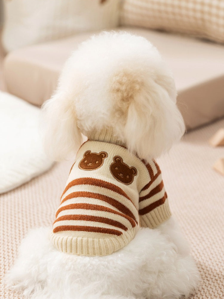 Back view of a white poodle wearing a cream and brown striped dog sweater with embroidered bear appliques