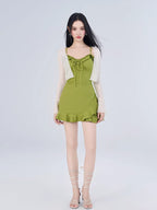 Full body shot of a woman in a green ruffled dress and white cardigan