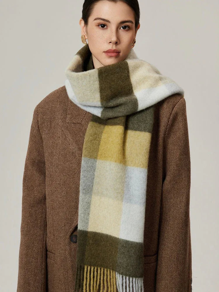 Side view of a woman wearing a neutral-toned plaid scarf with green, yellow, and grey blocks over a brown coat.