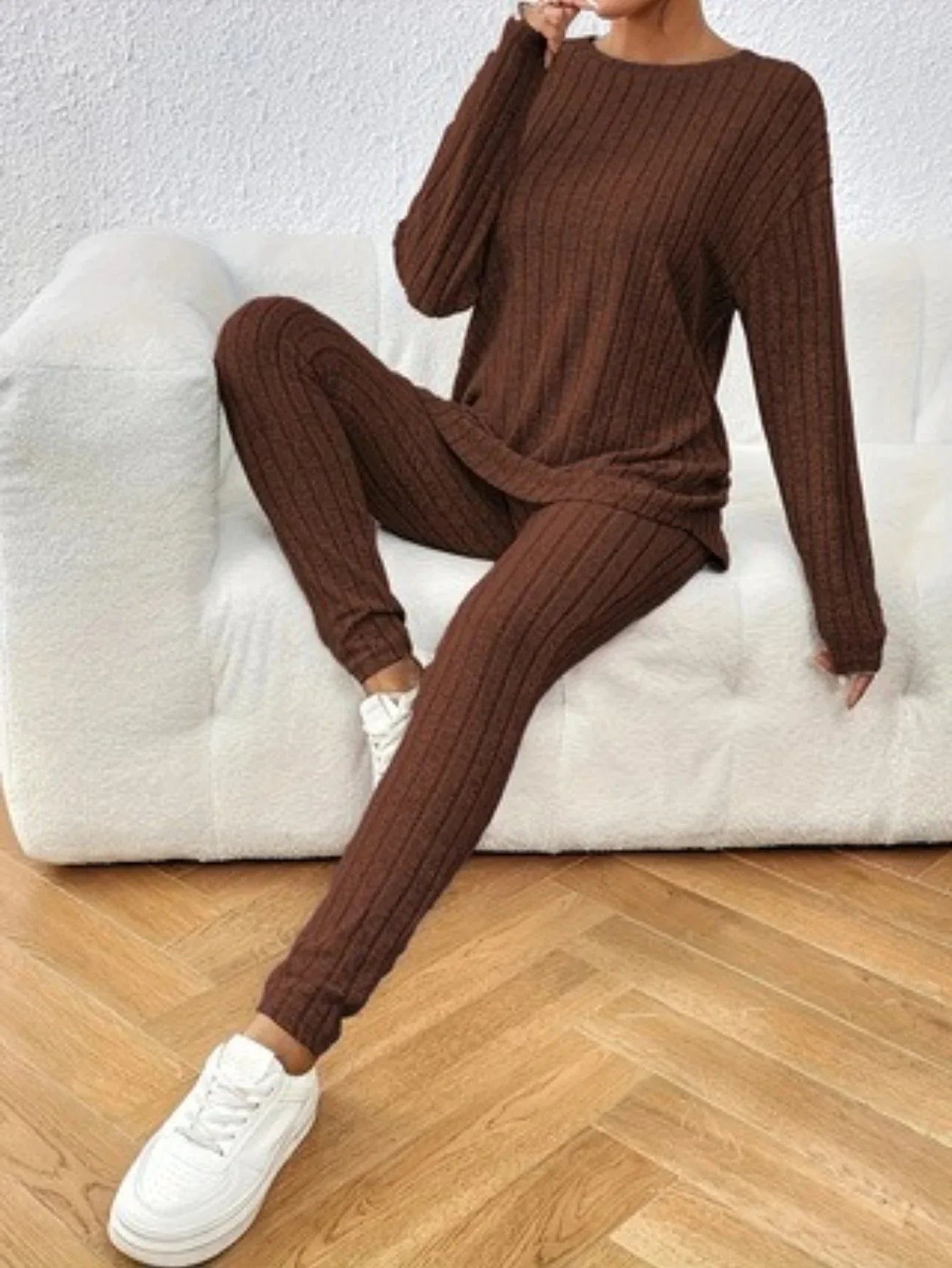 Woman wearing a brown ribbed knit loungewear set, sitting on a white couch.