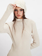 Close-up of a model wearing a cream ribbed turtleneck sweater and a cream knit beanie, with wet hair.