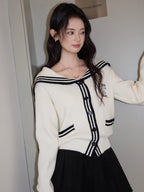 Woman in a white knit cardigan with a sailor collar, posing with her hand in her hair.