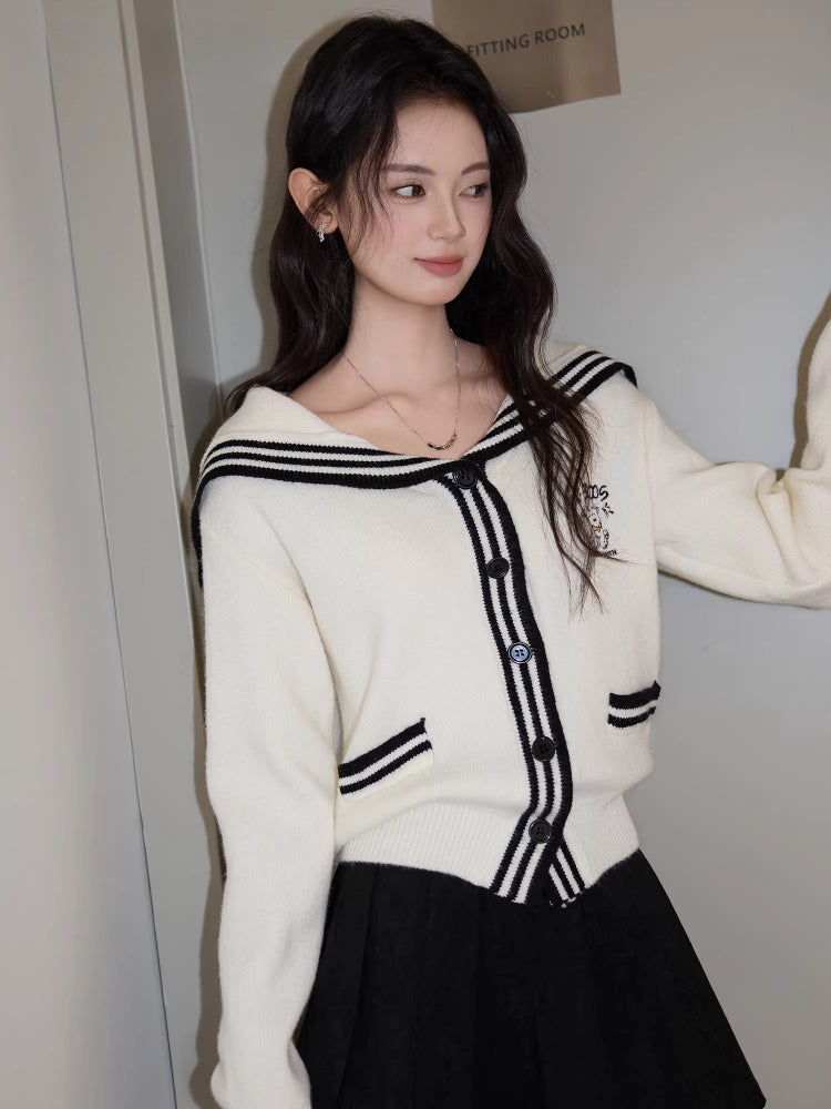 Woman in a white knit cardigan with a sailor collar, posing with her hand in her hair.