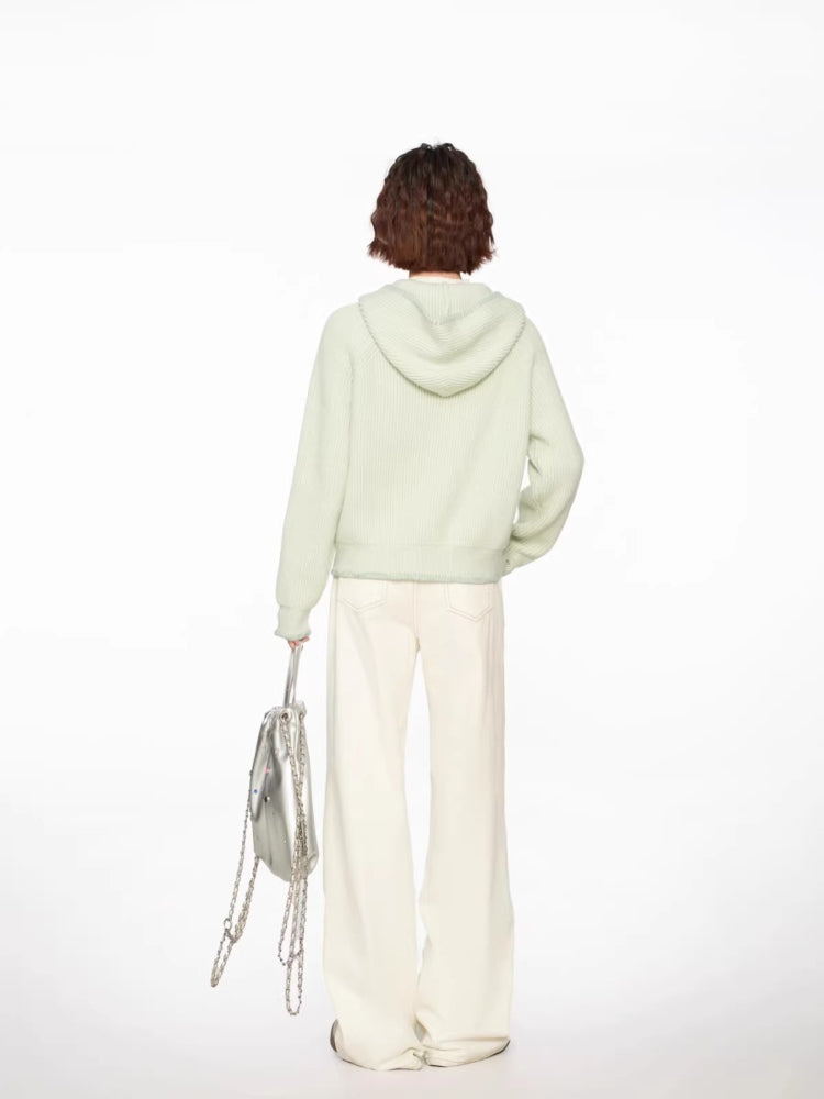 Woman wearing a light green hooded cardigan with white pants and a silver bag, full body back view