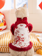 Rear view of a light-colored cat wearing a red and white traditional Chinese-style vest with floral embroidery and red faux fur trim.