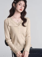 Woman wearing a beige ribbed knit cardigan with lace trim and a V-neck, with hands clasped.