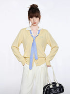 Full body shot of a woman in a yellow knit cardigan, white collared shirt, and cream wide-leg pants.