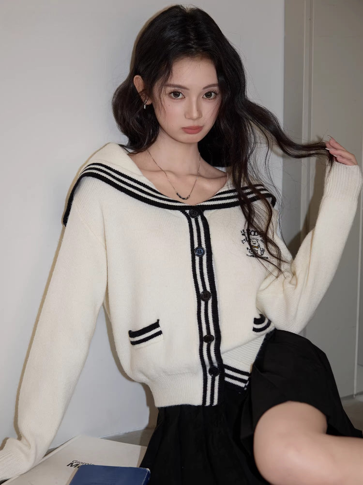 Close-up of a woman wearing a white knit cardigan with black trim and a sailor collar.