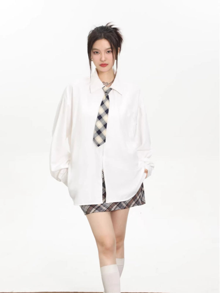 Model wearing an oversized white collared shirt with a checkered tie and a brown and grey plaid mini skirt.