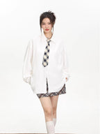 Model wearing an oversized white collared shirt with a checkered tie and a brown and grey plaid mini skirt.