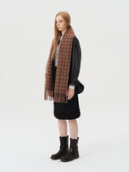 Side view of a woman wearing a brown plaid scarf, black leather jacket, and black skirt.