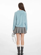 Back view of a model wearing a light blue fuzzy knit collared v-neck sweater with a grey pleated mini skirt.