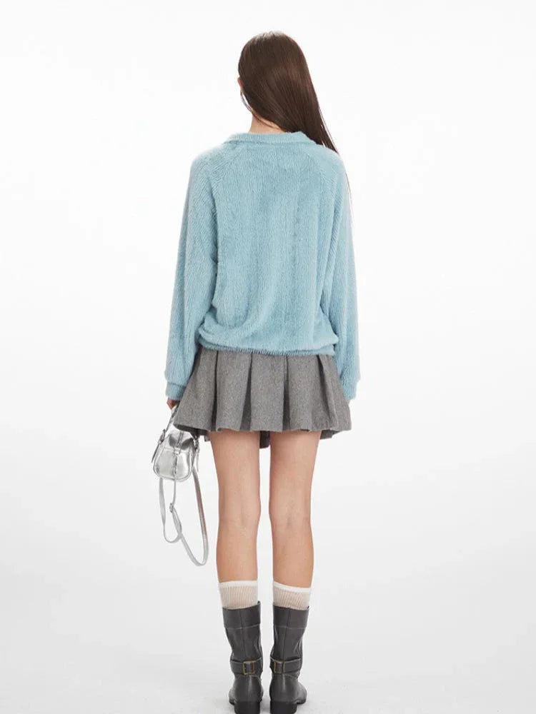 Back view of a model wearing a light blue fuzzy knit collared v-neck sweater with a grey pleated mini skirt.