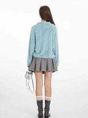 Back view of a model wearing a light blue fuzzy knit collared v-neck sweater with a grey pleated mini skirt.