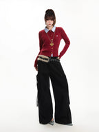 Woman posing in a red cable knit cardigan, light blue collared shirt, black cargo pants with a furry belt, and high heels.