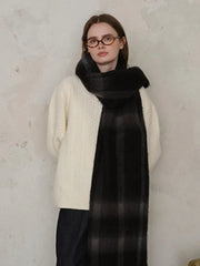 Woman wearing a cream cable-knit sweater and a dark plaid scarf with shades of grey.